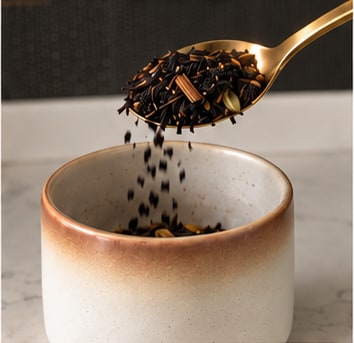 A spoonful of masala chai tipped into a ceramic mug