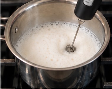 Hot milk frothed in the pan with a handheld frother