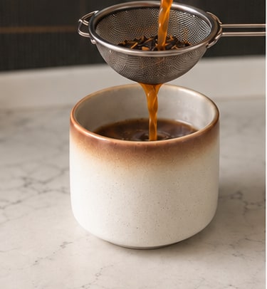 Steeped chai poured through a strainer into a cup